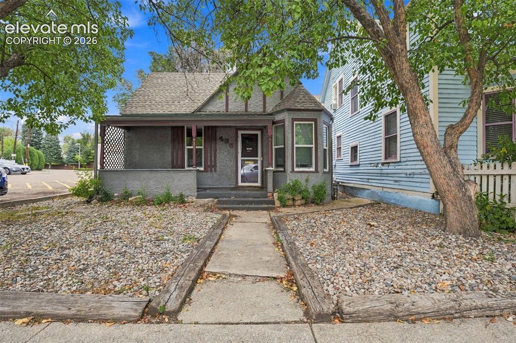 Image 34 of 34: Stone façade with a covered porch, bay window, and a gravel front yard