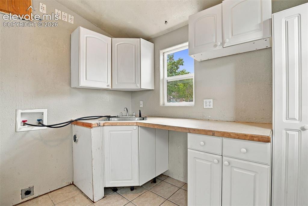 Image 5 of 34: White cabinetry with curved panel doors, corner sink, light-toned counterto