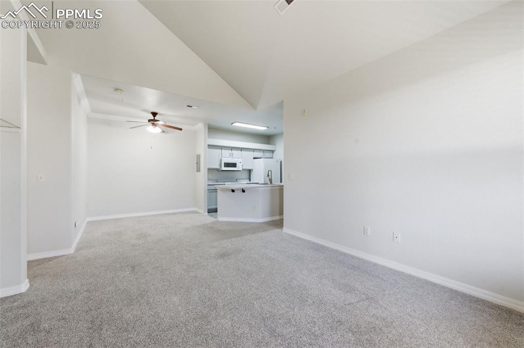 Image 24 of 39: Unfurnished living room with light carpet, ceiling fan, and high vaulted ce