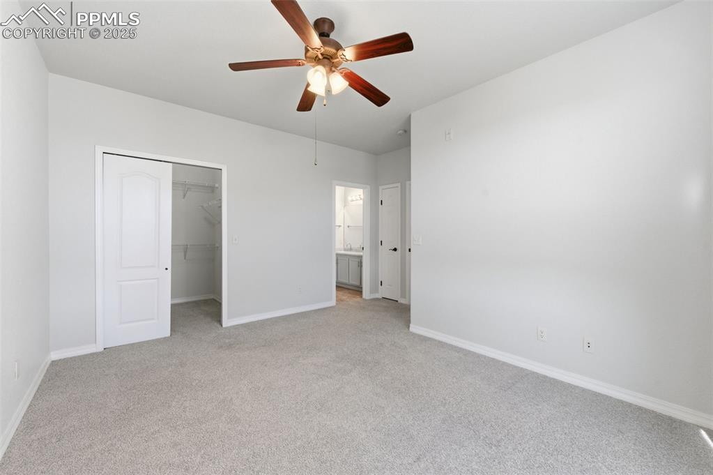 Image 27 of 39: Unfurnished bedroom with light carpet, a spacious closet, and ceiling fan