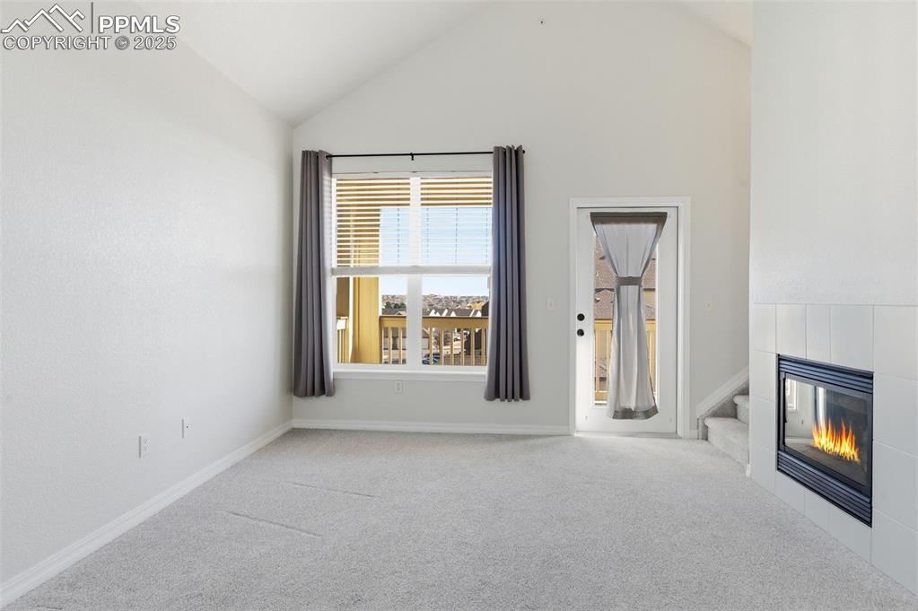 Image 7 of 39: Unfurnished living room featuring carpet, a fireplace, stairway, and high v