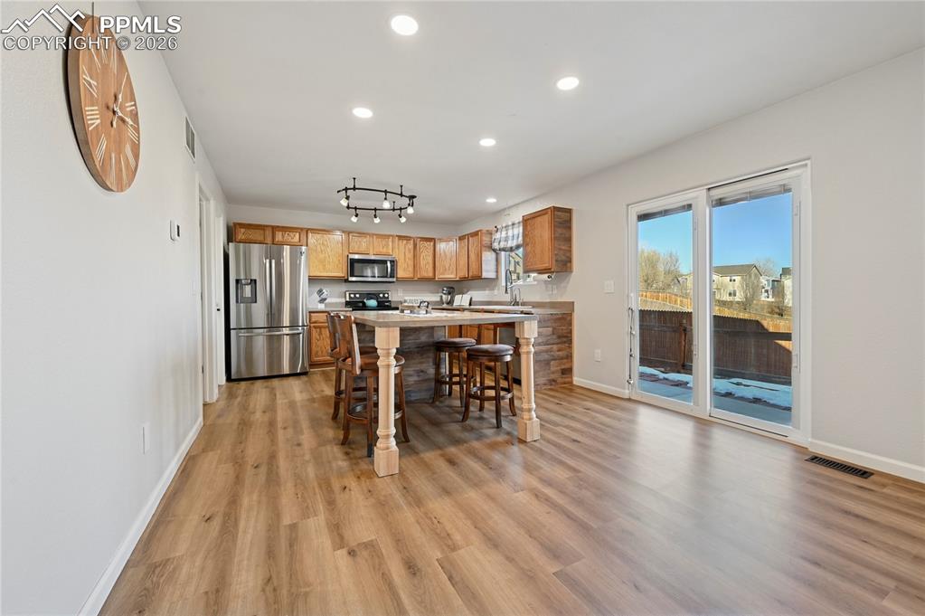 Image 10 of 37: Kitchen with light countertops, brown cabinetry, a kitchen bar, appliances