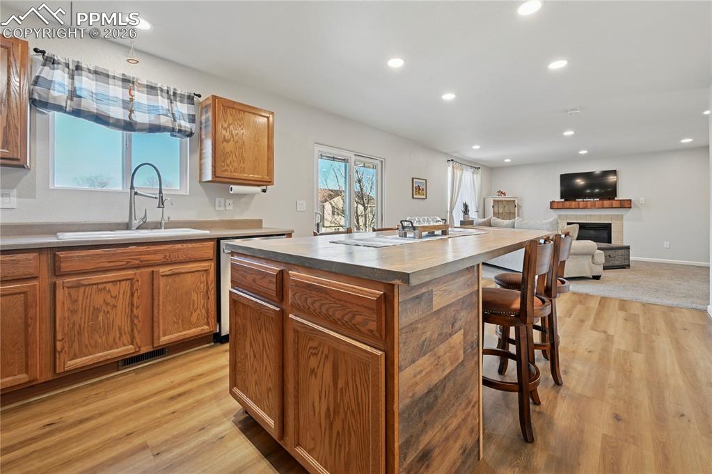 Image 11 of 37: Kitchen with a tiled fireplace, brown cabinets, open floor plan, a kitchen