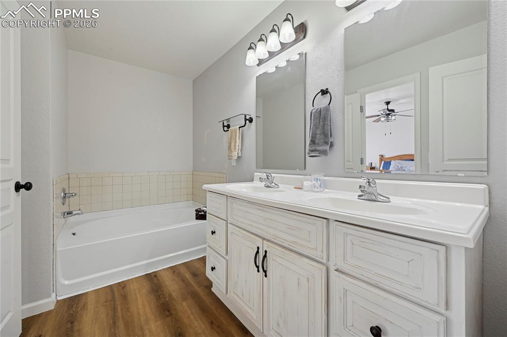 Image 19 of 37: Full bathroom featuring double vanity, dark wood-style floors, a bath, and