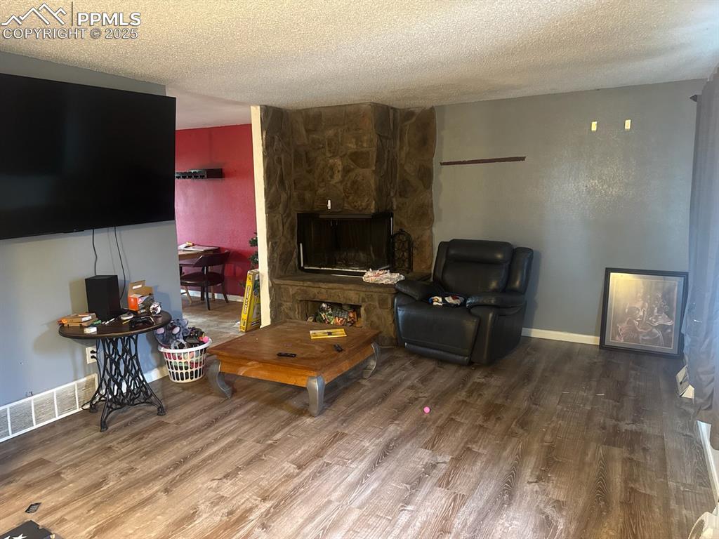 Image 3 of 6: Living room with a textured ceiling, wood finished floors, and a stone fire