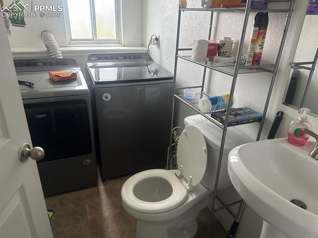 Image 4 of 6: Bathroom with a textured wall, washer and clothes dryer, and dark tile patt