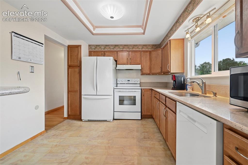Image 11 of 50: Well-appointed kitchen featuring wood cabinetry, white appliances, durable