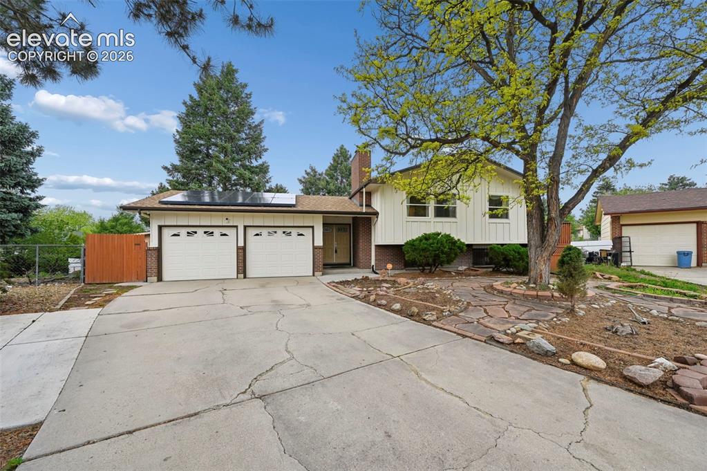 Image 2 of 50: Split-level residence featuring a two-car garage with panel doors, a brick