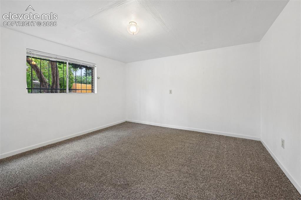 Image 26 of 50: Carpeted room with white walls, a single window featuring security bars, an