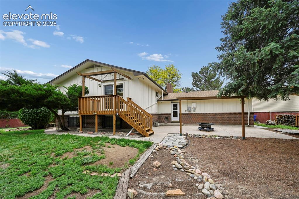 Image 3 of 50: Rear exterior featuring a wood deck with stairs, a patio area, and a covere