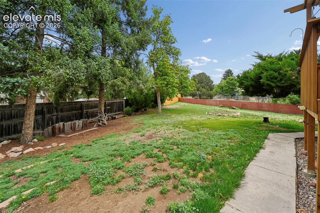 Image 47 of 50: Expansive backyard featuring mature trees, partial wood fencing, and a conc