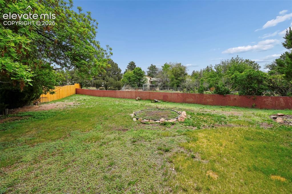 Image 49 of 50: Expansive rear yard featuring a partial wood fence, mature tree, and a ston