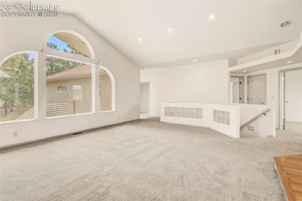 Image 12 of 35: Unfurnished living room featuring light colored carpet, lofted ceiling, and