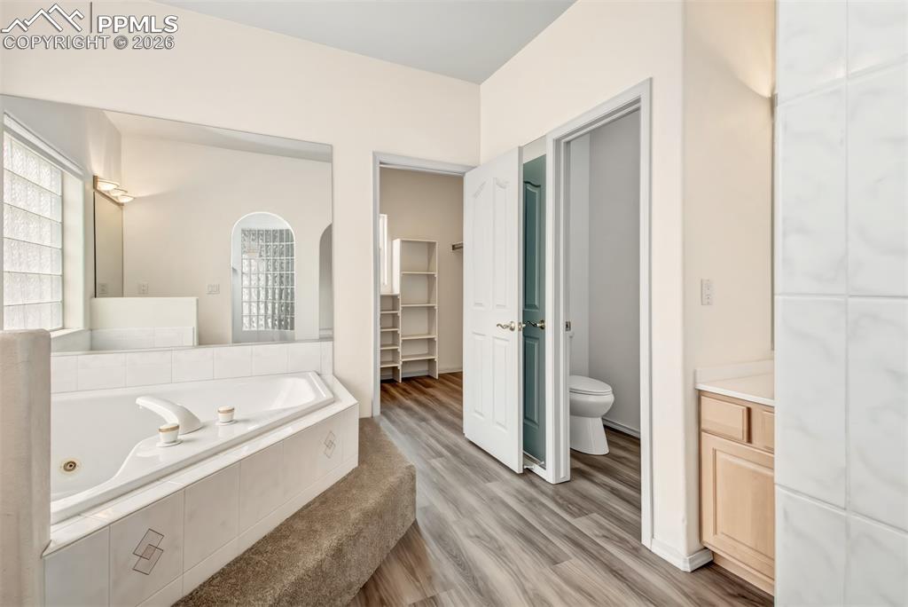 Image 22 of 35: Bathroom featuring a walk in closet, a whirlpool tub, and light wood-style 