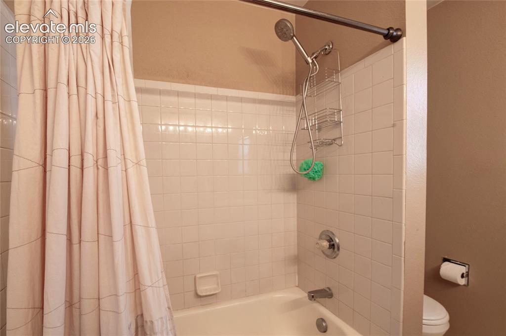 Image 18 of 34: Bathtub with white subway tile surround, chrome fixtures, and a shower curt
