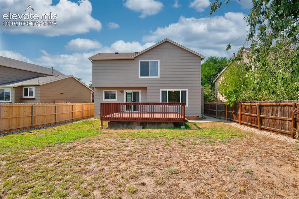 Image 33 of 34: Rear exterior featuring a spacious wood deck, two sliding glass doors, and 