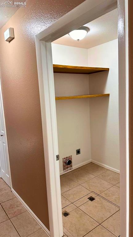 Image 13 of 34: Laundry area featuring light tile patterned flooring, a textured wall, hook