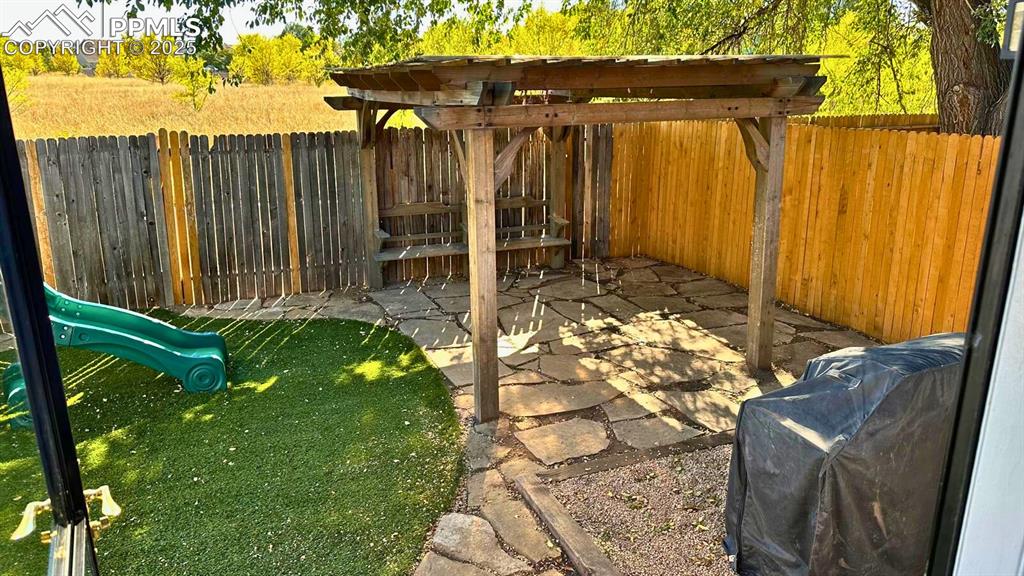 Image 28 of 34: Fenced backyard featuring a playground and a pergola patio area