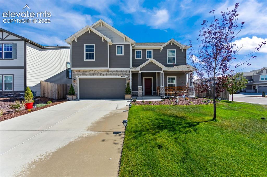 Caption: Two-story residence featuring a gray exterior, stone facade accents, an attached garage, a covered f