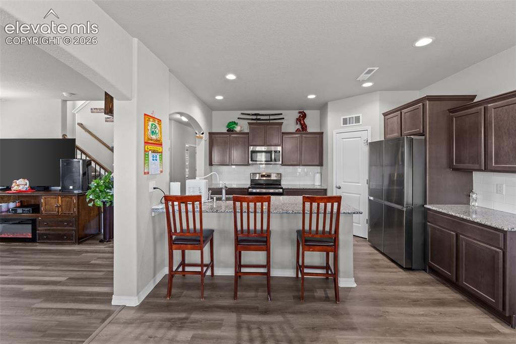 Image 10 of 41: Kitchen featuring wood-finish flooring, dark wood cabinetry, stainless stee