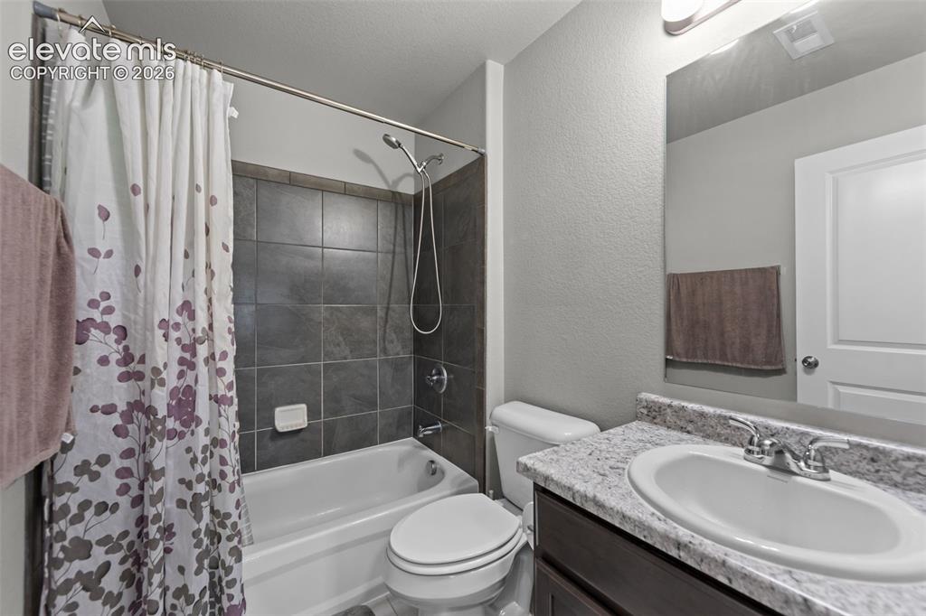 Image 23 of 41: Bathroom featuring a bathtub with dark tiled surround, white toilet, vanity