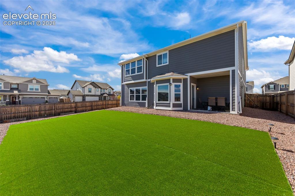 Image 28 of 41: Fenced backyard with artificial turf, gravel pathways, covered patio, and m