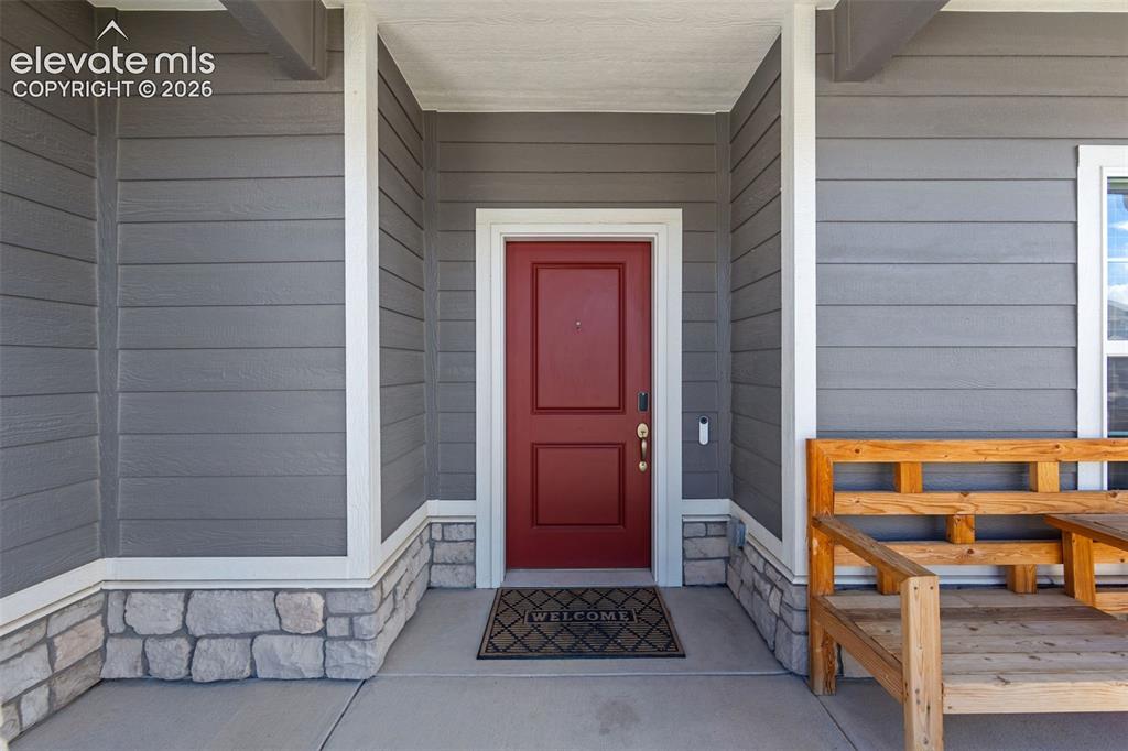 Image 4 of 41: Welcoming red entry door, gray siding, stone accent base, and concrete porc
