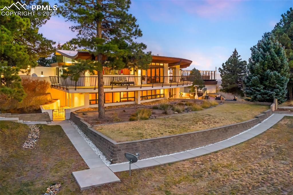 Image 2 of 39: Back of house at dusk featuring a lawn, stucco siding, and a balcony