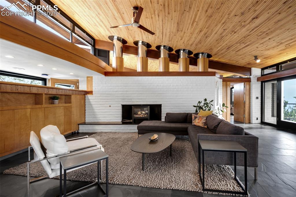Image 7 of 39: Living area featuring a brick fireplace, ceiling fan, and wood ceiling