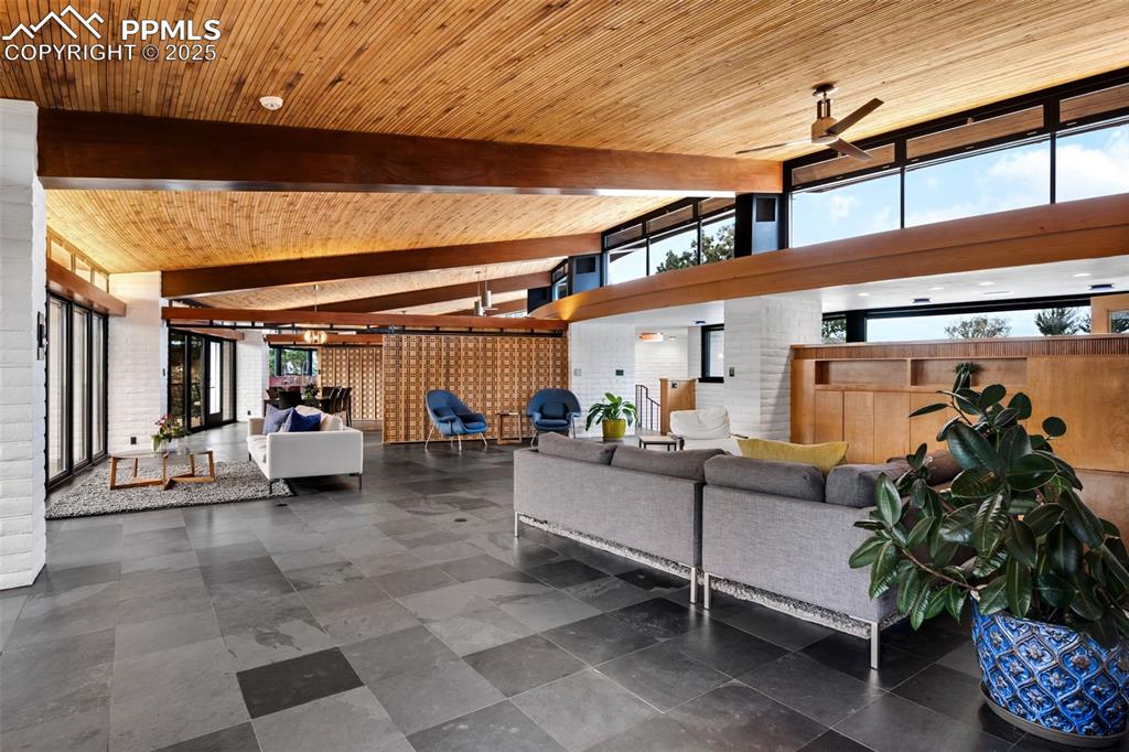 Image 8 of 39: Living area with a wall of windows, wooden ceiling, and a ceiling fan