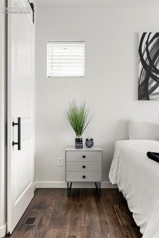 Image 21 of 38: Bedroom with dark wood-style flooring and a barn door