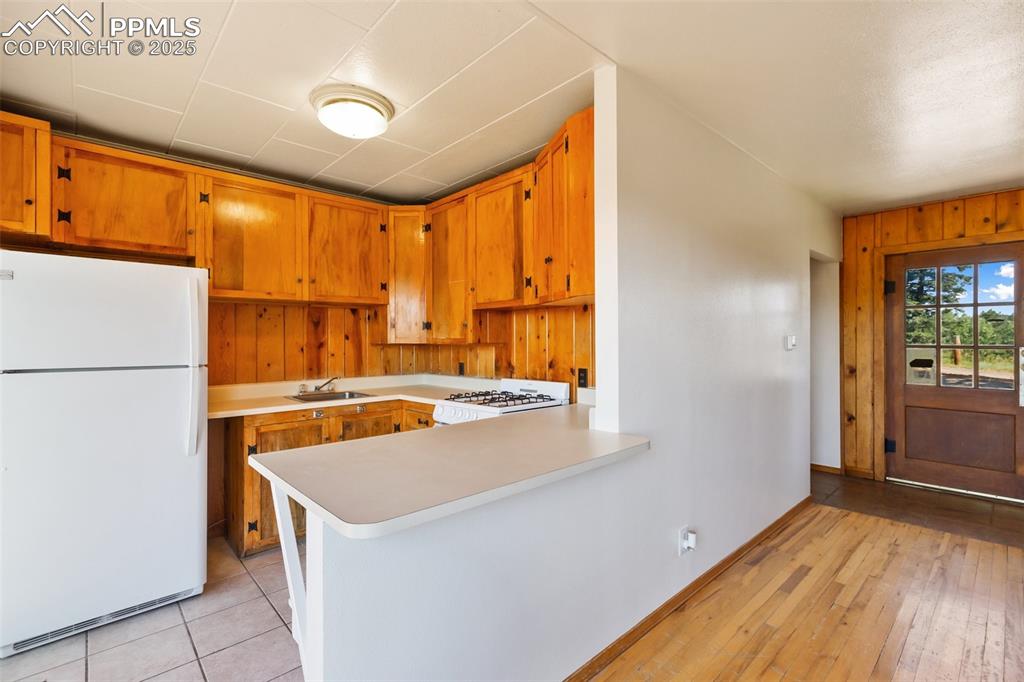 Image 14 of 35: Kitchen with freestanding refrigerator, light countertops, brown cabinets,