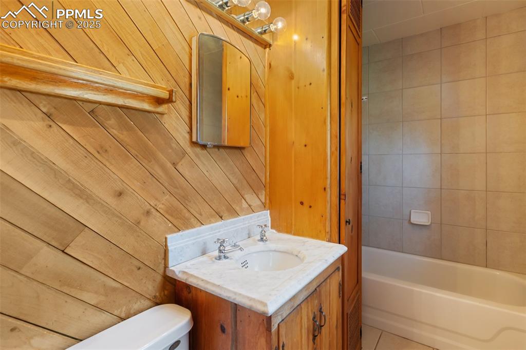 Image 28 of 35: Full bathroom with vanity, wood walls, and tile patterned flooring
