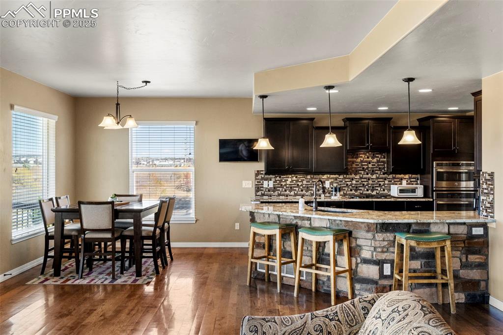 Image 13 of 41: Kitchen featuring pendant lighting, dark brown cabinets, backsplash, dark w