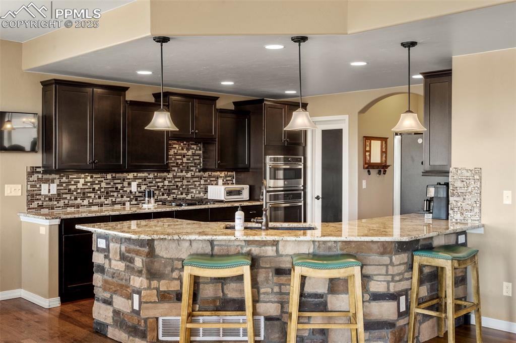 Image 14 of 41: Kitchen featuring backsplash, a breakfast bar, dark brown cabinets, a penin