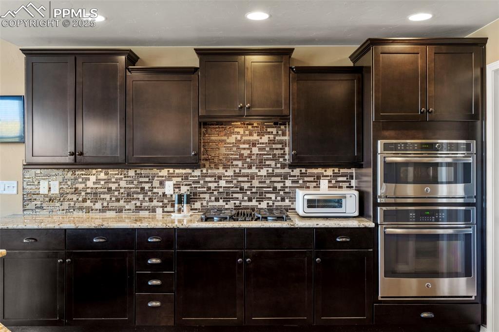 Image 18 of 41: Kitchen featuring backsplash, dark brown cabinetry, appliances with stainle