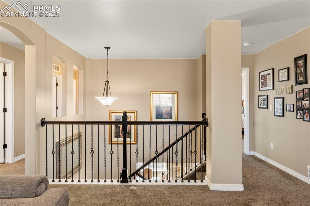 Image 31 of 41: Hallway with an upstairs landing, carpet floors, and arched walkways