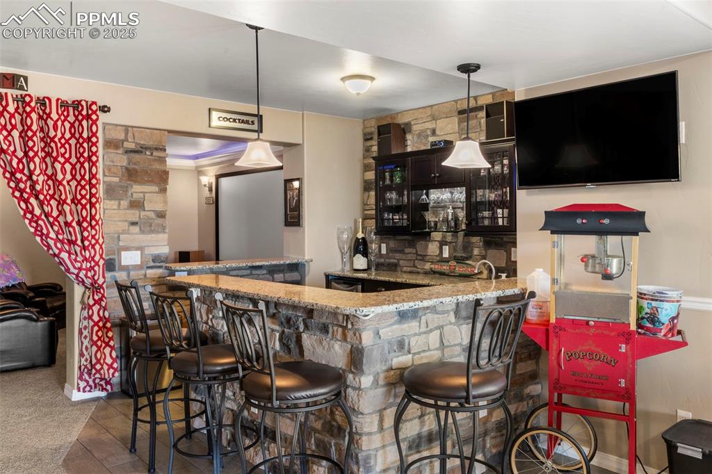 Image 39 of 41: Indoor wet bar with decorative light fixtures, light stone counters