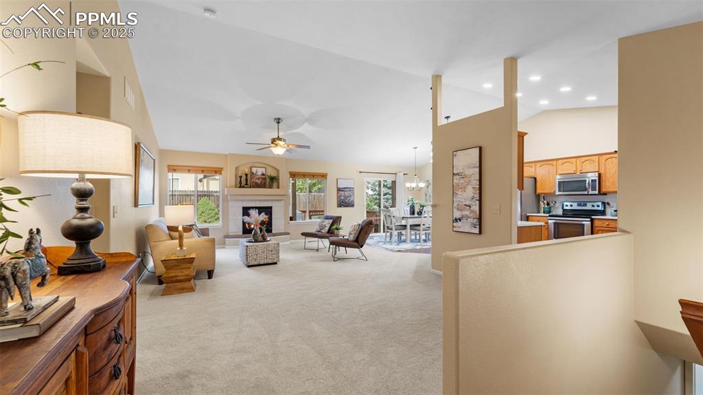 Image 7 of 33: Living area with light colored carpet, a tiled fireplace, ceiling fan, high
