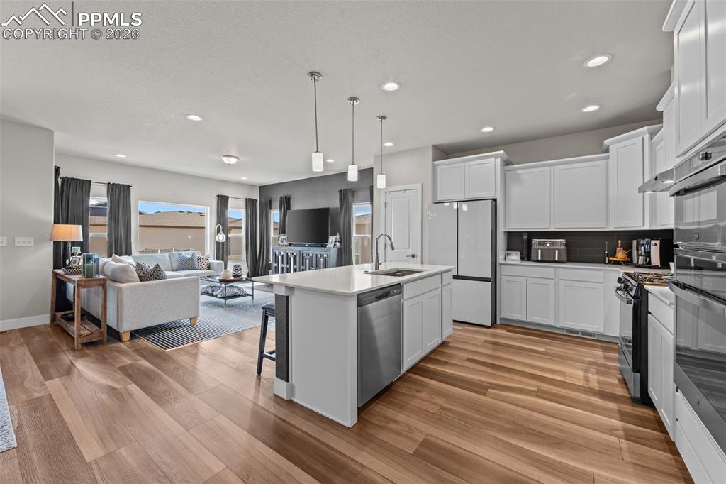 Image 12 of 49: Open-concept kitchen featuring white cabinetry, stainless steel appliances,