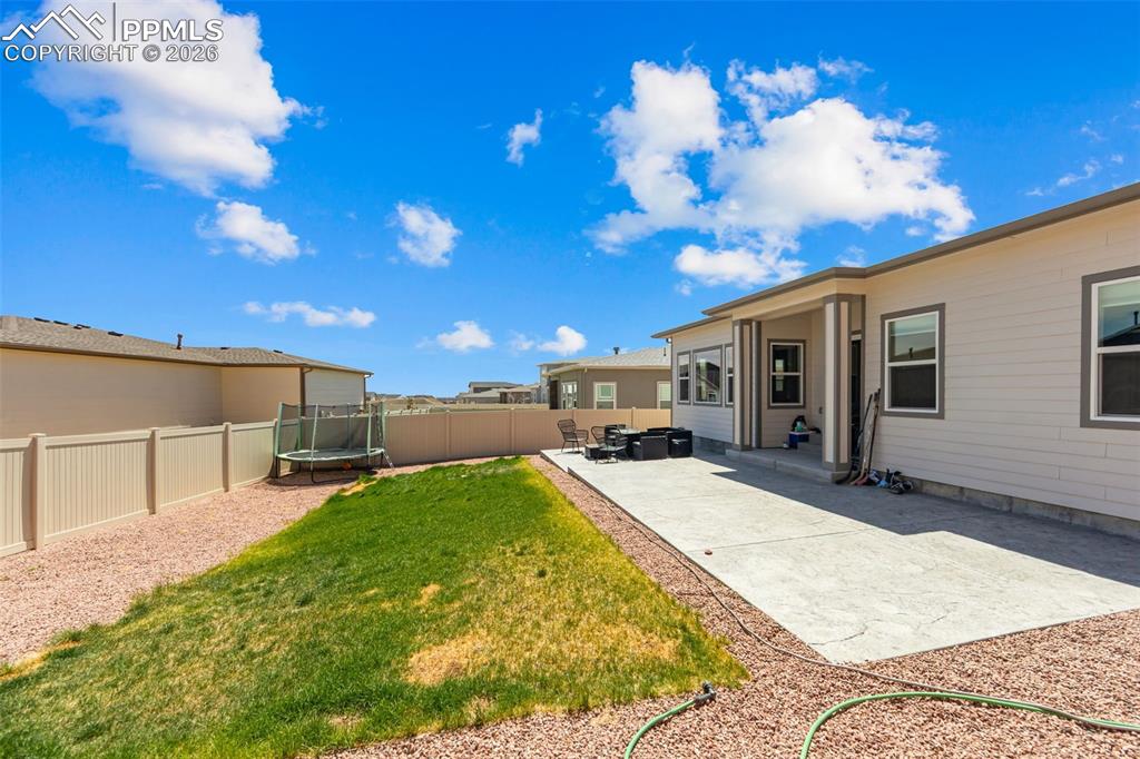 Image 37 of 49: Expansive backyard featuring a large concrete patio, manicured lawn, and de
