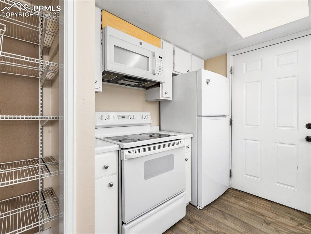 Image 10 of 28: Kitchen featuring white appliances, white cabinets, dark wood-style floorin