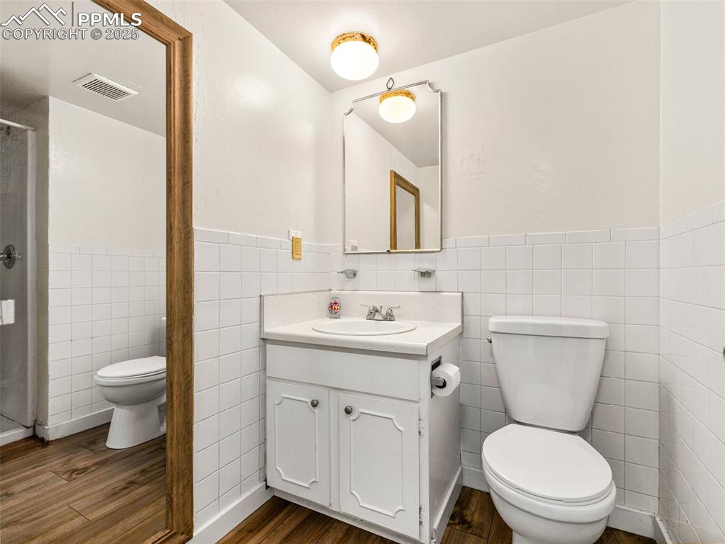 Image 12 of 28: Full bathroom featuring tile walls, vanity, dark wood finished floors, a wa