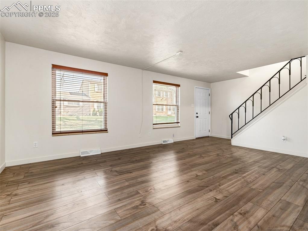 Image 7 of 28: Unfurnished living room featuring stairway, wood finished floors, and a tex