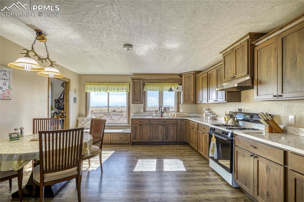 Image 15 of 50: Kitchen with range with gas stovetop, wood finish cabinetry, dark wood-styl