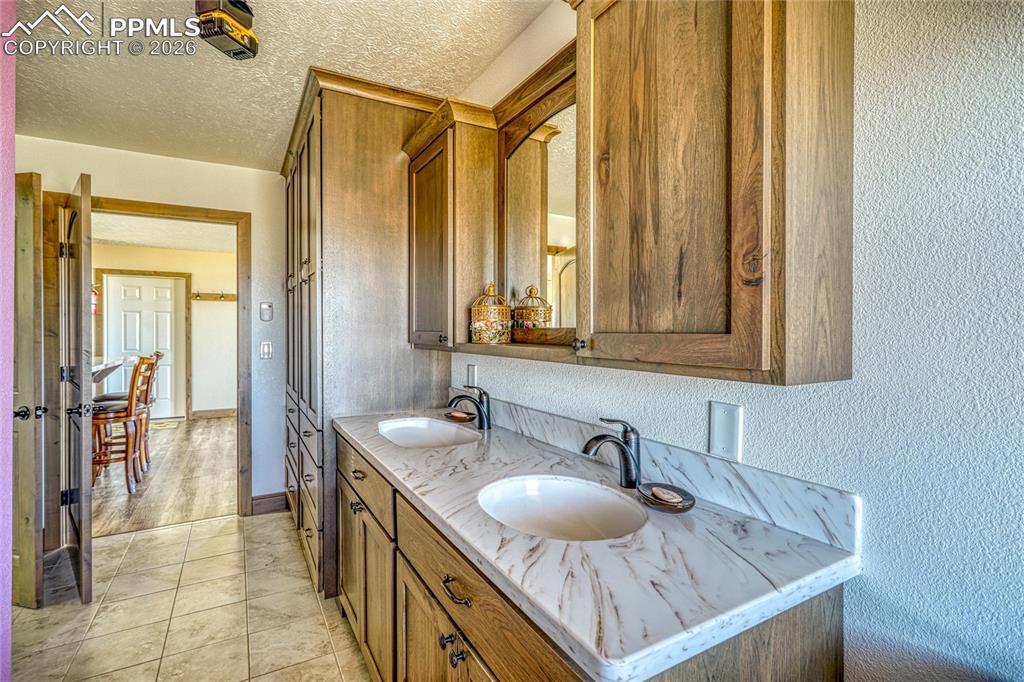 Image 27 of 50: Full bathroom with double vanity, a textured wall, and a textured ceiling