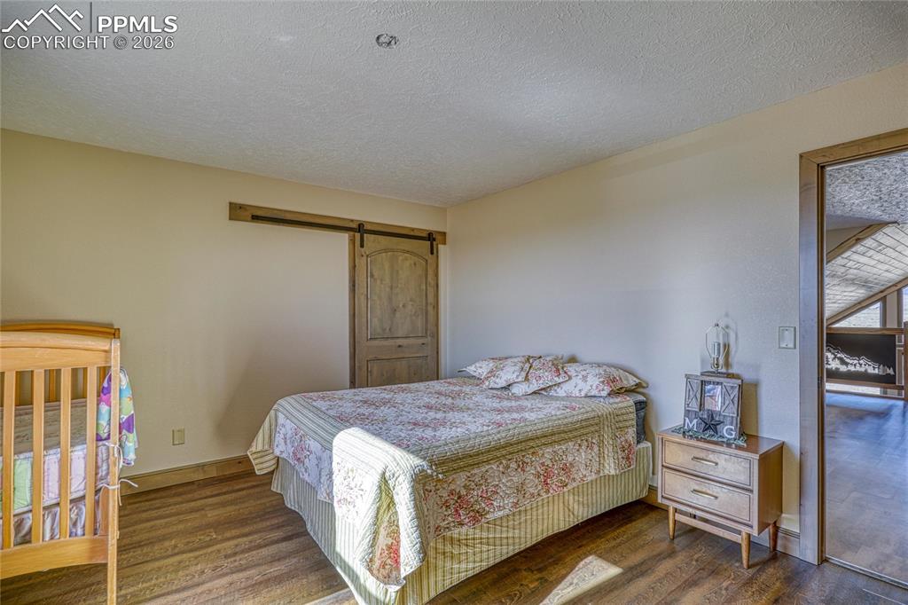 Image 33 of 50: Bedroom featuring a textured ceiling, dark wood-style flooring, and a barn