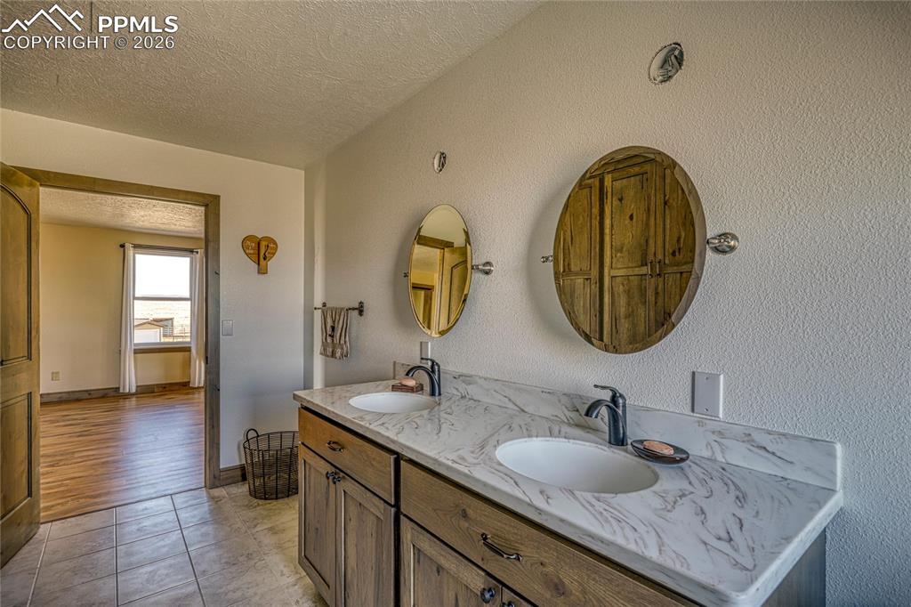 Image 39 of 50: Bathroom with double vanity, a textured ceiling, light tile patterned floor