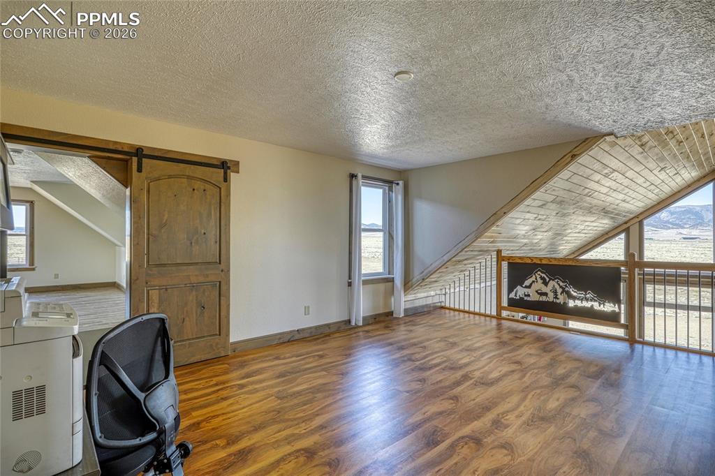 Image 40 of 50: Unfurnished office with a barn door, dark wood-type flooring, plenty of nat
