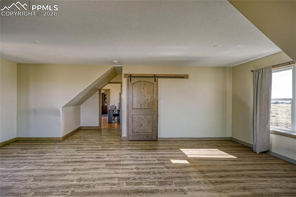 Image 42 of 50: Additional living space with a barn door, light wood-type flooring, and a t